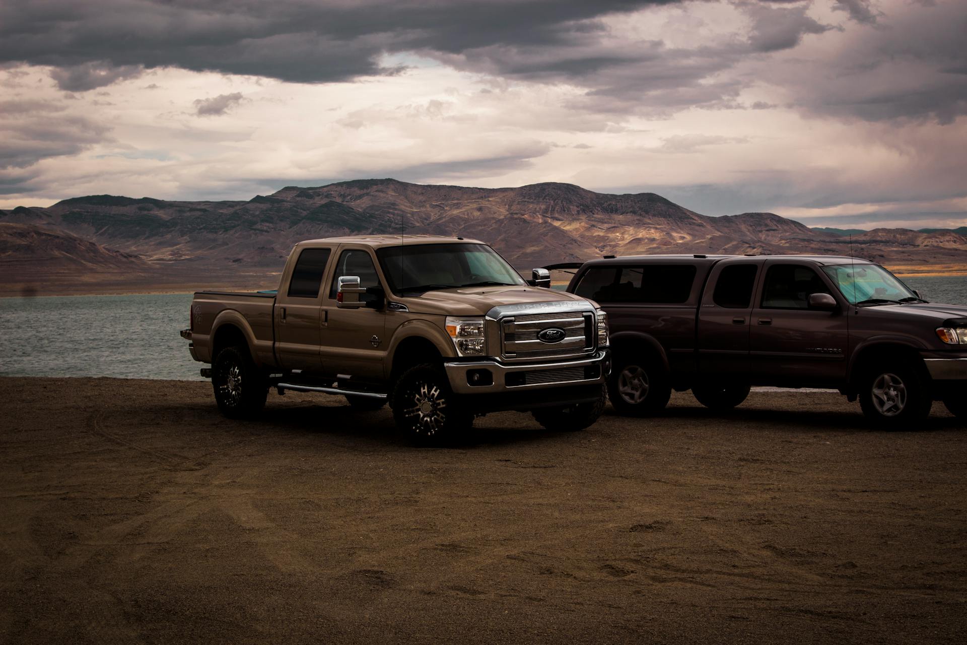 Two heavy duty pickup trucks parked by a mountain lake
